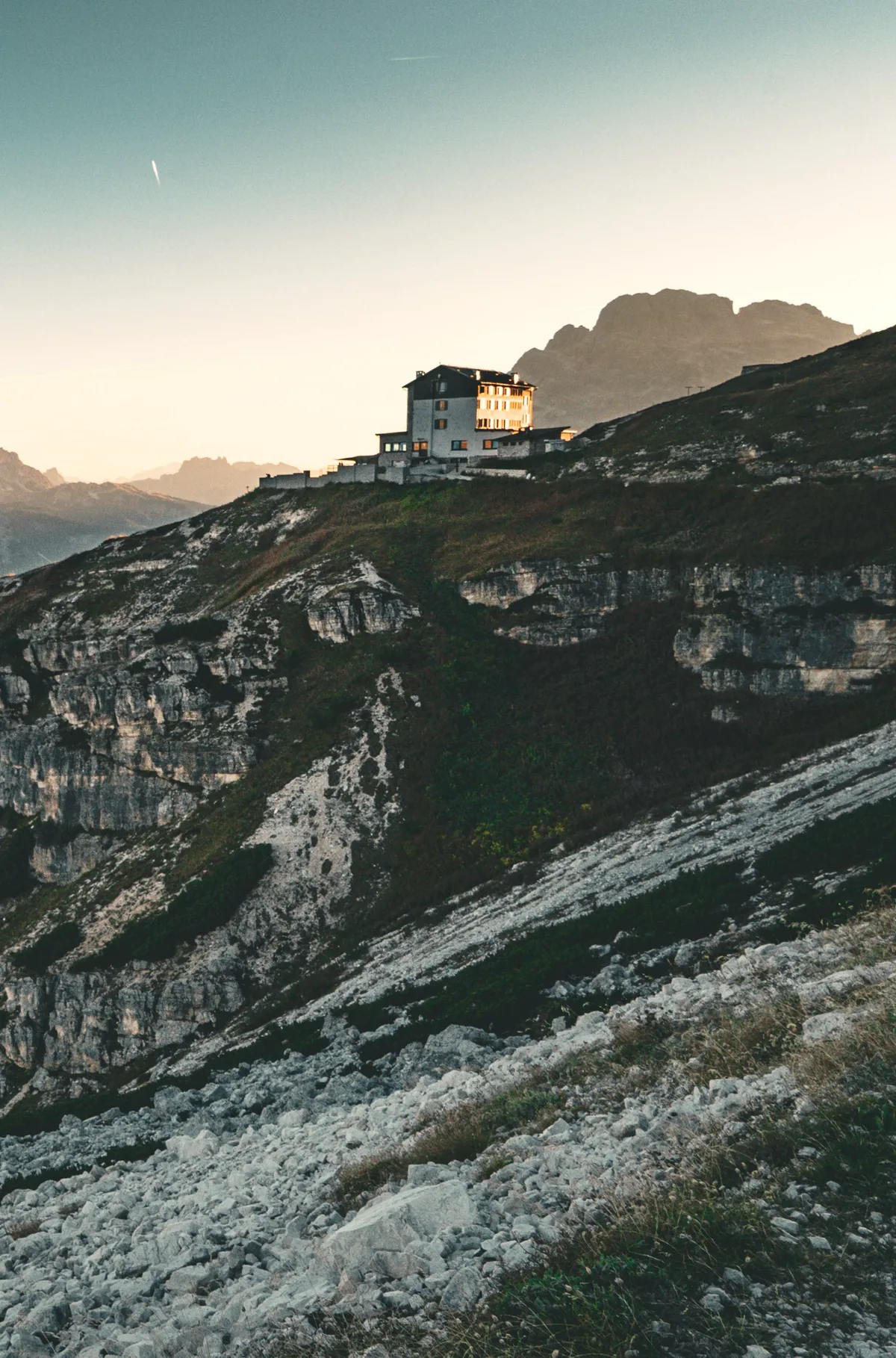 A stone mountain refuge on an open Dolomite ridge, lit by first light